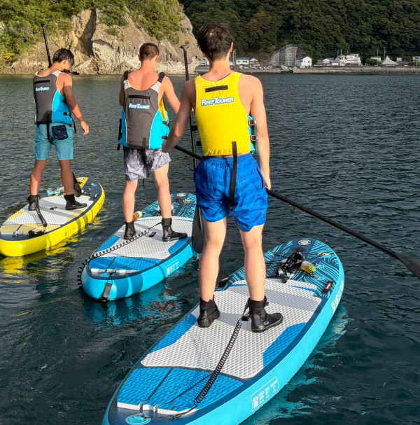 体幹バツグンのバレー部男子たちがSUPボードの上に立ち、夕方の海を進む様子
